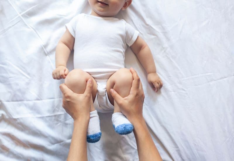 Bố mẹ có thể kích thích ruột hoạt động bằng cách giữ hai đầu gối trẻ, gập từ từ chân phải về phía vai phải rồi duỗi chân phải thẳng, lặp lại tương tự với chân trái. 