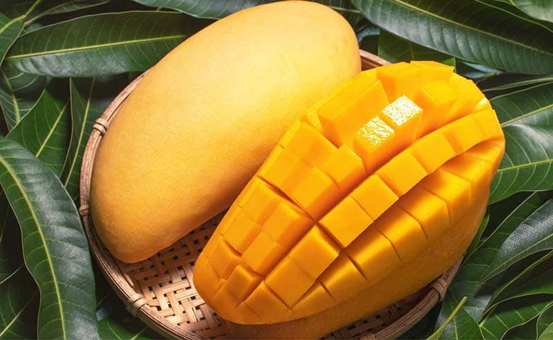 Xoài chín cắt hạt lựu và xoài nguyên quả đặt trên lá xoài.