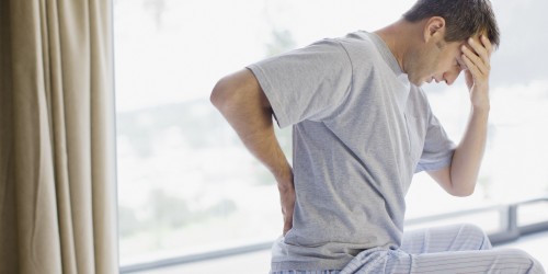 Man sitting on bed with backache and headache