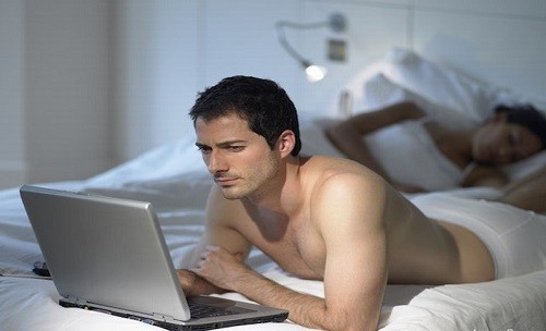 Man using laptop as wife sleeps