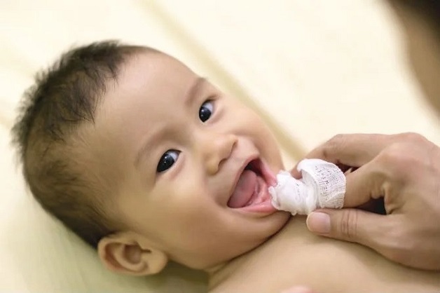 Mẹ nên sử dụng bông hoặc gạc mềm thấm với nước mát và thực hiện massage nhẹ nhàng quanh vùng nướu để giảm sưng nướu.