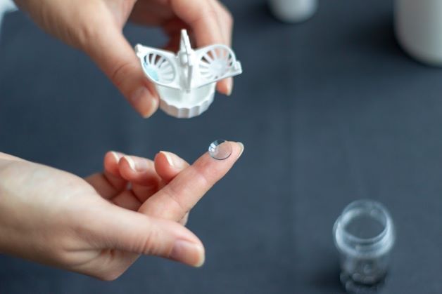 Dùng ngón tay trỏ thuận để đặt kính sau đó nhỏ nước mắt nhân tạo vào lòng kính. Sử dụng tiếp tay còn lại mở to hai mí mắt, sau đó nhẹ nhàng đặt kính vào trong mắt.